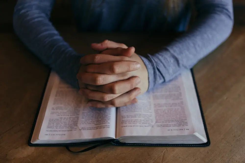person with folded hands on a bible